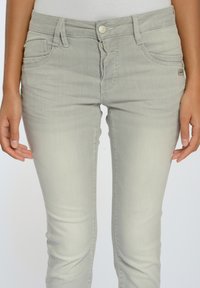 Ljusgrå denimjeans med slim fit, framfickor och knappstängning. Materialet har en slät yta med minimal detaljering.