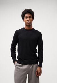 Pulover negru din tricot cu guler rotund, fit slim, mâneci lungi și tiv din tricot. Prezintă detalii subtile cu logo pe piept.