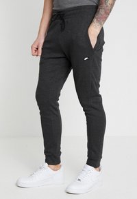 Grå joggerbyxor i mjukt tyg, med sidofickor, dragsko i midjan och en liten vit logotyp på vänster höft.