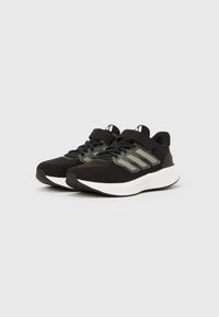 Fekete sportcipők fehér talppal, fűzővel és tépőzáras pánttal, szürke oldalsávokkal, egyszerű világos háttéren elhelyezve.