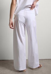 Weiße weit geschnittene Hosen aus leichtem Stoff. Minimales Design mit zwei Gesäßtaschen und einer glatten Textur.