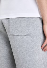 Šedé tepláky vyrobené z měkké, texturované tkaniny mají zadní kapsu s viditelným šitím. Pas je elastický pro pohodlí.