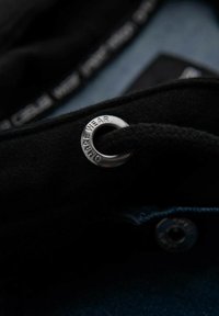 Tessuto nero con un occhiello in metallo argento e cordino. Texture e materiali notevoli migliorano il dettaglio visivo complessivo.