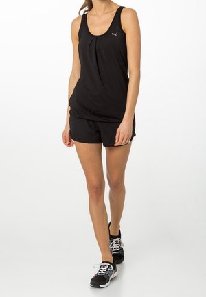Top deportivo negro sin mangas con un frente plisado, combinado con pantalones cortos negros texturizados y zapatillas negras con acentos de color.