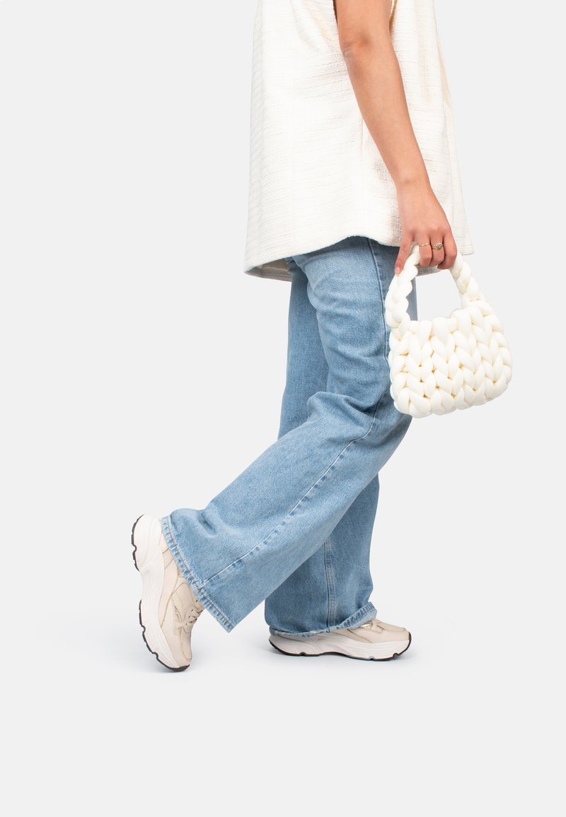 Sac à main tissé blanc avec un design chunky, porté par une personne vêtue d'un haut beige ample et d'un jean bleu clair, associé à des baskets claires.