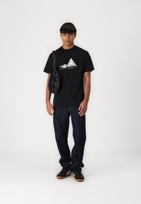Sort bomuld t-shirt med et grafisk design af en vintage bil og trekantsformer; parret med mørke jeans og sorte sneakers.