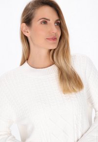 Pulover alb tricotat, cu un model texturat ce include diamante ridicate și cabluri, guler rotund și mâneci lungi. Stoff neted, aspect cald.