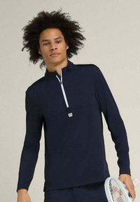 Pullover sportivo blu navy a maniche lunghe con mezzo zip, zip bianca e piccolo logo bianco sul petto. Tessuto morbido e leggero.