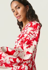 Vestido floral rojo con patrones blancos, con mangas largas y escote en V profundo. La tela parece suave y ligera.