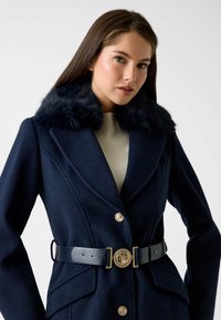 Marineblauwe wolblend jas met een faux fur kraag, een ceintuur in de taille, grote gouden knopen en opgestikte zakken met gestructureerde stof.