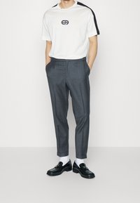 Vit t-shirt med svarta axelinslag och broderad logotyp, kombinerad med grå skräddarsydda byxor och svarta loafers med spänne.