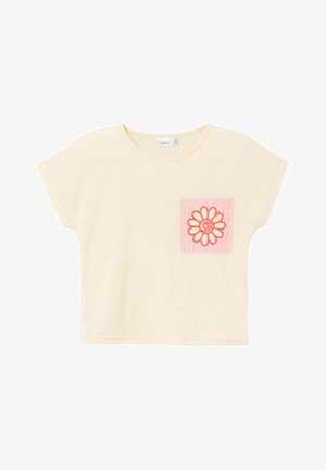 T-shirt en coton beige clair à manches courtes, avec une poche en éponge rose ornée d'un contour rouge en forme de fleur.