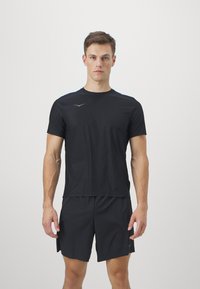 Camiseta atlética negra de manga corta, con cuello redondo y un detalle de logo sutil. Combinada con pantalones cortos negros a juego, ambos hechos de un tejido ligero.