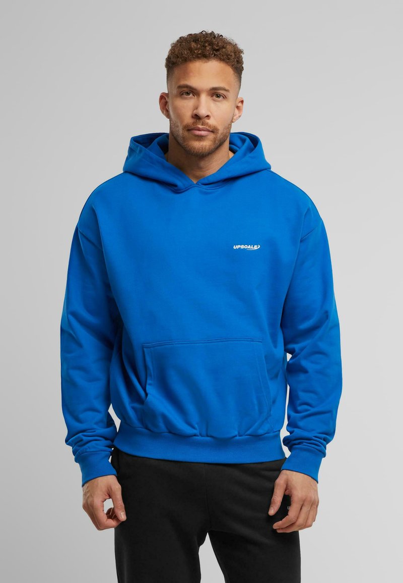 Sudadera con capucha azul, con bolsillo frontal, puños y dobladillo acanalados. Logo dorado "UPSOALE" en el pecho. Textura suave y corte casual.