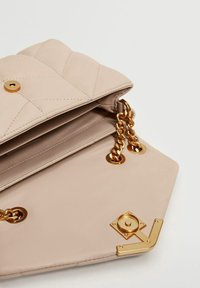 Sac à main en cuir matelassé beige avec bandoulière chaîne dorée, fermeture à pression et détail décoratif en métal doré à l'avant.