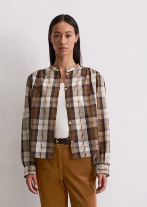 Bruine geruite blouse met lange mouwen, ronde kraag en elastische manchetten. Een wit onderhemd en bruine corduroybroek maken de outfit compleet.