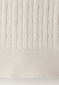 Tissu tricoté couleur crème avec motif torsadé vertical au-dessus de la bordure côtelée.