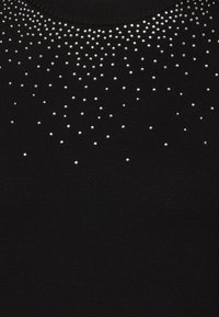 Pull noir à encolure ronde, orné d'un dégradé de strass argentés sur la partie supérieure. Tissu doux et texturé.