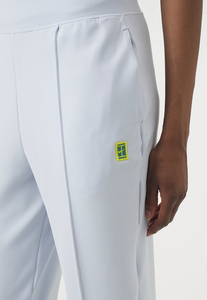 Himmelblaue Sporthose mit glatter Textur, ausgestattet mit einem gelben rechteckigen Logo im Bereich der linken Tasche und maßgeschneiderten Nähten.