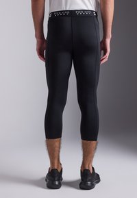 Schwarze, athletische Leggings mit einer taillierten Passform, ausgestattet mit einem Logo-Bund, kürzerer Länge und glattem, dehnbarem Material.