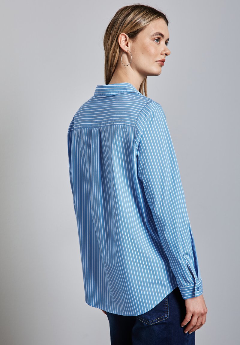 Camicia azzurra chiara con maniche lunghe e bottoni, caratterizzata da strisce verticali bianche, una spalla posteriore e polsini fissati con bottoni. Texture liscia.