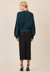 Niebieskozielony sweter w prążki z szerokimi rękawami, połączony z czarną midi spódnicą dżinsową ozdobioną małymi srebrnymi akcentami i bocznym rozcięciem, uzupełniony czarnymi szpilkami.