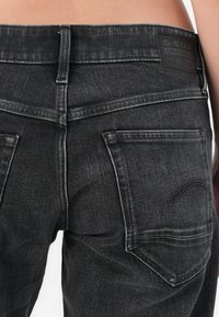 Dettaglio in primo piano di jeans neri in denim sul retro con tasche visibili, dettagli della cucitura, passanti per cintura e un'etichetta G-Star Originals.