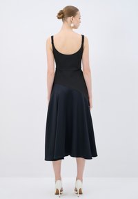 Schwarzes Kleid mit tailliertem Oberteil und fließendem, asymmetrischem Saum in tiefem Marineblau. Texturierte Träger und eine glatte, satinähnliche Oberfläche.