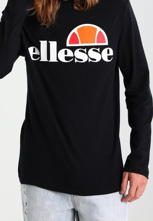 Person trägt ein schwarzes Langarmshirt mit einem großen halbkreisförmigen Logo in Orange und Rot sowie dem Schriftzug "ellesse" auf der Brust, kombiniert mit hellen Jeans.