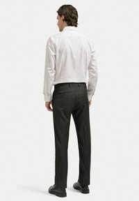 Vit skjorta med krage, grå dressbyxor, svarta skor. Skjortan har lång ärm; byxorna har bakfickor och en skräddarsydd passform.