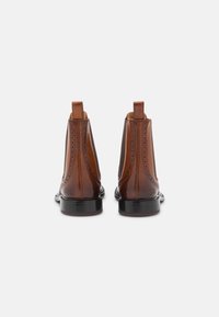 Bottines Chelsea en cuir marron avec une finition lisse, des détails en brogue le long des coutures, des panneaux latéraux en élastique et un petit talon empilé.