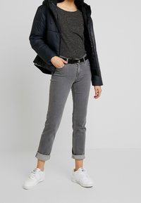 Chaqueta de plumas negra, top gris, jeans grises con detalles de botones y zapatillas blancas. El conjunto presenta un diseño ajustado con puños enrollados.