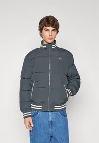 Chaqueta bomber acolchada en gris oscuro con acentos de rayas blancas. Cuenta con un alto cuello, cierre frontal y bolsillos laterales.