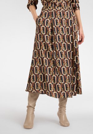 Multikleurige, gestreepte midi-rok met een donkere achtergrond en geometrische vormen in bruin, beige en groen, gedragen met beige kniehoge laarzen.