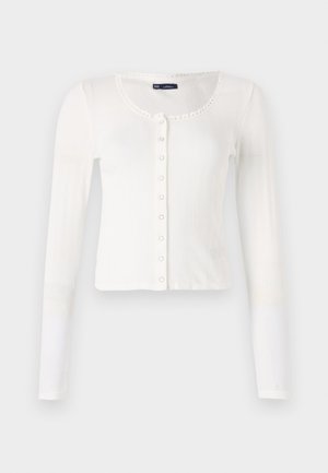 White long-sleeve cardigan with ribbed texture, round neckline, and decorative trim. Features a row of small buttons down the front.