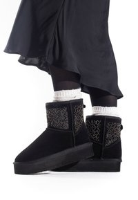 Botas de tobillo de ante negro con acentos de cuentas texturizadas en los lados y suela de goma plana, combinadas con calcetines de punto blancos.