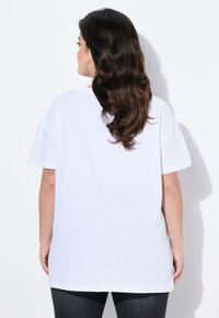 Camiseta blanca de manga corta con un corte relajado, diseño simple, textura suave y aberturas laterales, combinada con jeans de mezclilla oscura.