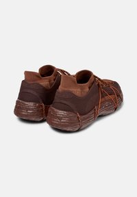 Bruna sportskor med en texturerad sula och elastiska snören, som visar en tight passform och ventilerande meshmaterial vid hälen.