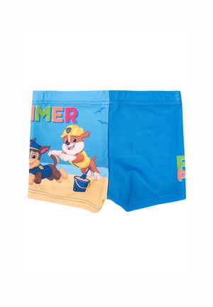 Costumi da bagno blu con personaggi animati sulla parte frontale, con la scritta "ESTATE" sopra e un design colorato su uno sfondo di spiaggia sabbiosa.