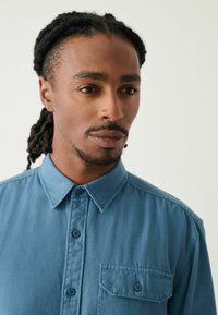 Lichtblauw overhemd met een spread collar, een borstzak en een gladde stoftextuur. Kenmerkt zich door twee knopen op de kraag en subtiele stikdetails.