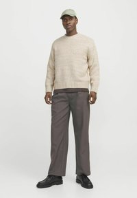 Beige knitted sweater with ribbed hem, paired with gray tailored trousers. Black lace-up shoes and a light green cap complete the outfit.