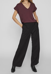 Weinrotes V-Ausschnitt-T-Shirt mit umgeschlagenen kurzen Ärmeln, kombiniert mit schwarzen weit geschnittenen Hosen. Die Schuhe sind schwarze spitze Knöchelstiefel.