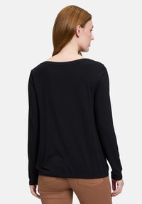 Schwarzes langärmliges Shirt mit weiter Ausschnittkante, aus weichem Stoff, mit lockerer Passform und schlichtem Design, sichtbaren Nähten am Saum.