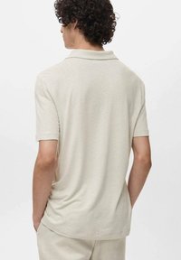 Camisa polo beige de manga corta, con un cuello clásico y una tela suave y texturizada. La parte trasera presenta un ajuste relajado y un dobladillo recto.