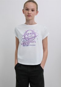 Tricou alb din bumbac cu mâneci suflecate, având o grafică mov cu o bilă de discotecă și un craniu, textul fiind "Visit Scalper's Disco."
