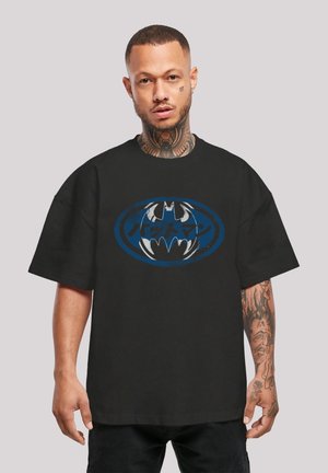 Black cotton t-shirt featuring a large blue and white Batman logo with Japanese text. Short sleeves and loose fit. Textured fabric.