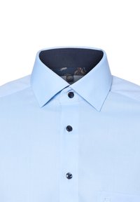 Camicia button-up di colore azzurro chiaro con un tessuto testurizzato, presenta un interno del colletto scuro, due bottoni neri e una tasca sul lato sinistro.