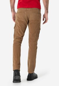 Bruine corduroy cargo broek met zijzakken, voorzien van een slim fit ontwerp. Gedragen met zwarte schoenen en een rode top.