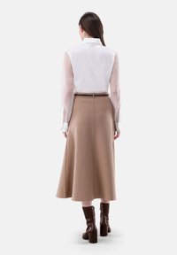 Blusa bianca a maniche lunghe con maniche trasparenti, abbinata a una gonna beige a trapezio. La gonna ha una texture liscia e arriva sotto il ginocchio. Stivali con tacco marroni.