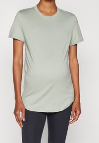 Camiseta verde claro hecha de tela suave, con mangas cortas y escote redondeado, que presenta un corte relajado y un dobladillo curvado.